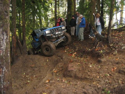1990 Ford Bronco - Modified off-road vehicle navigates a challenging muddy incline with spectators observing.