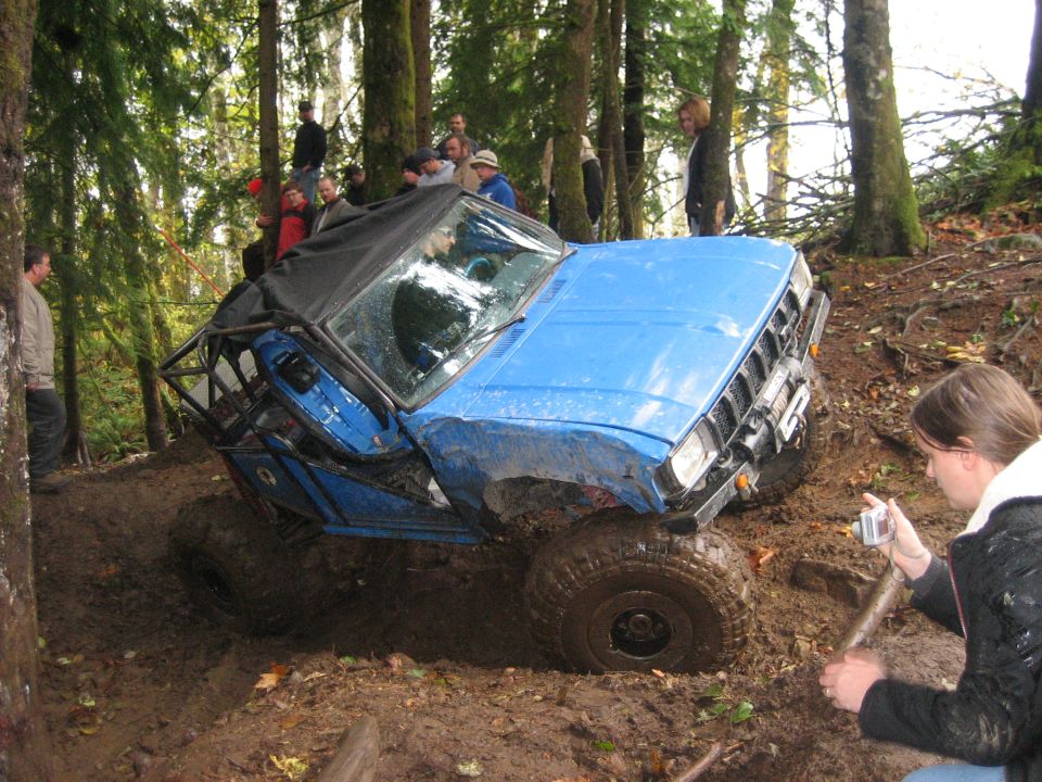 Blue off-road vehicle stuck in mud, with a roll cage and soft top