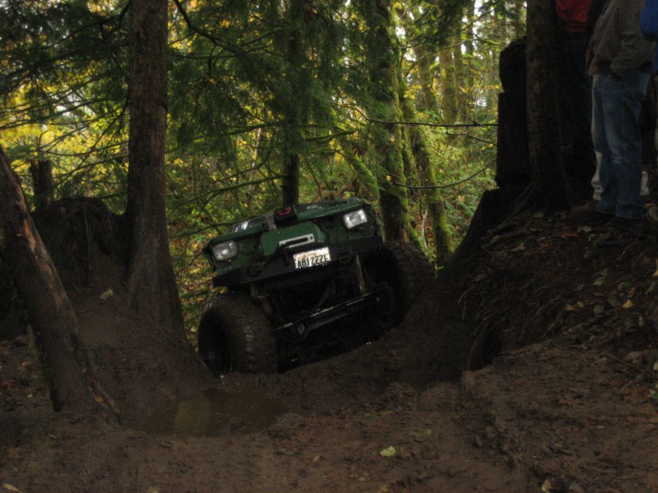 Green 1990 Ford Bronco climbing a muddy hill, front view