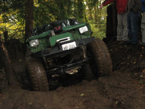 1990 Ford Bronco - Off-road vehicle navigating a muddy trail, showing its front end and large tires.