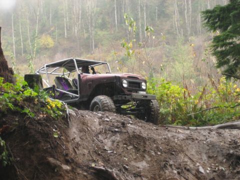 1990 Ford Bronco - Off-road vehicle navigates a steep, muddy trail surrounded by trees.