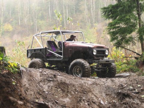 1990 Ford Bronco - A custom off-road vehicle navigates a challenging muddy trail in a wooded area.