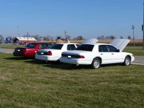 1997 Mercury Grand Marquis - Three 1997 Mercury Grand Marquis sedans are parked on a grassy field under a clear blue sky.