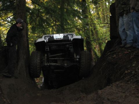1990 Ford Bronco - An off-road vehicle navigates a challenging muddy terrain surrounded by trees.