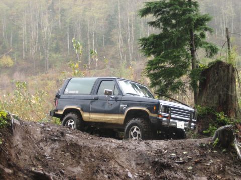 1990 Ford Bronco - A Ford Bronco II navigates a challenging muddy terrain with a wooded background.