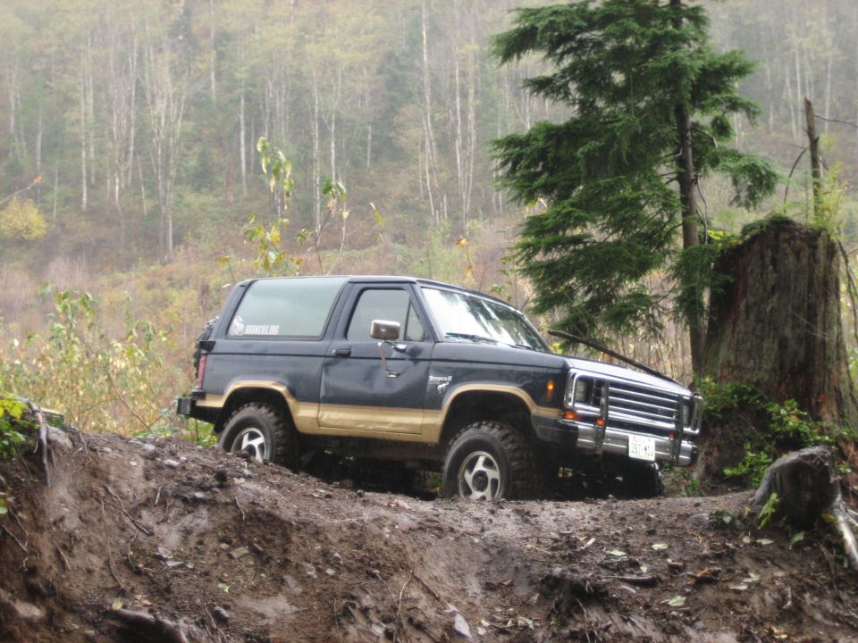 Dark blue and tan Ford Bronco II off-roading on a muddy hill