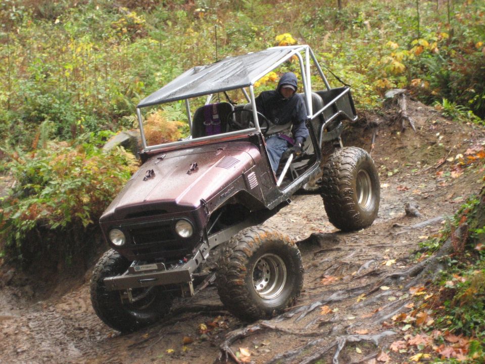 Maroon Toyota Land Cruiser FJ40 off-roading on a muddy trail with large tires and a roll cage