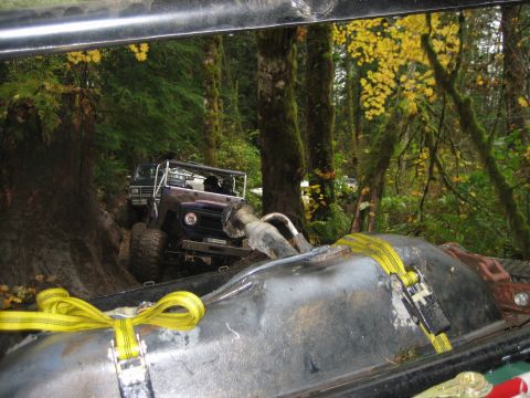 1990 Ford Bronco - Off-road vehicles navigate a muddy trail through a forest with yellow autumn leaves.