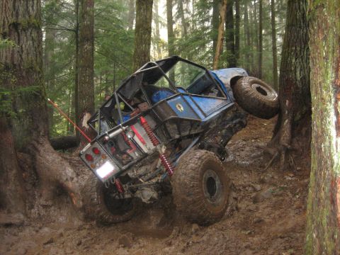 1990 Ford Bronco - Off-road buggy navigating a muddy trail in a forest, leaning heavily against a tree.