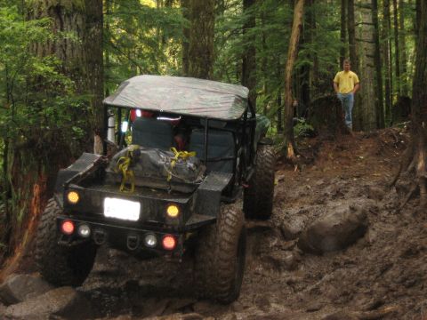 1990 Ford Bronco - This heavily modified off-road vehicle navigates a challenging, muddy path through a dense forest.
