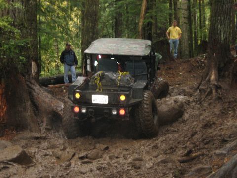 1990 Ford Bronco - An off-road vehicle struggles through a muddy forest path with two onlookers.