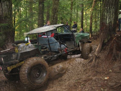 1990 Ford Bronco - This heavily modified off-road vehicle navigates a challenging muddy terrain with onlookers observing.