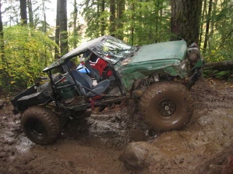 1990 Ford Bronco - This heavily modified off-road vehicle is stuck deep in the mud on a wooded trail.