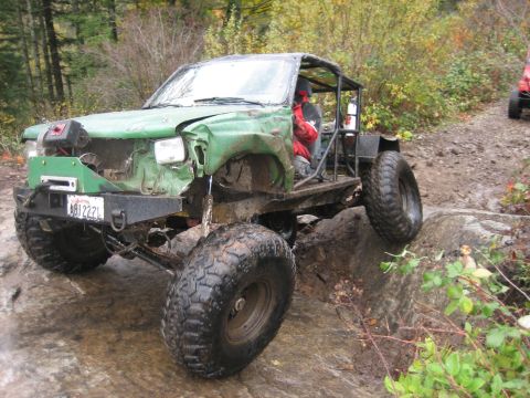 1990 Ford Bronco - A heavily modified off-road vehicle navigates a challenging rocky terrain with another vehicle visible in the background.