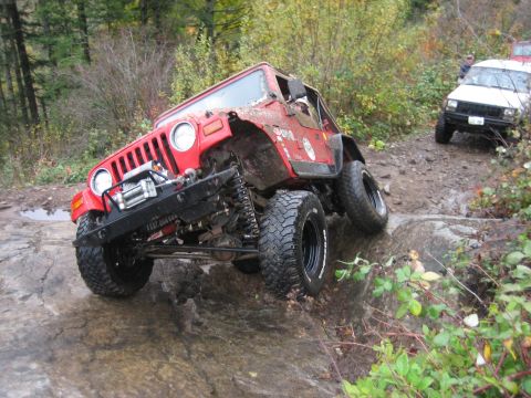 1990 Ford Bronco - Red Jeep Wrangler navigating a difficult rocky off-road course with a white Jeep Cherokee following.