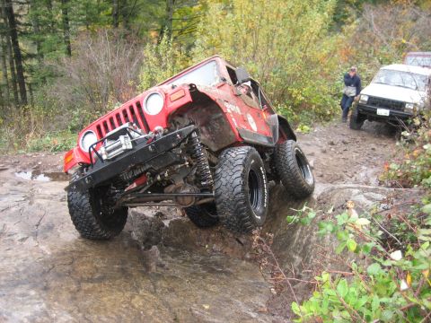 1990 Ford Bronco - A red Jeep Wrangler navigates a difficult rocky terrain on an off-road trail.