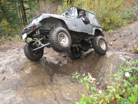 1990 Ford Bronco - A modified Jeep Wrangler navigates a difficult rocky terrain on an off-road trail.