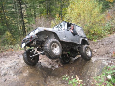 1990 Ford Bronco - A driver maneuvers a modified Jeep Wrangler over challenging terrain on an off-road trail.