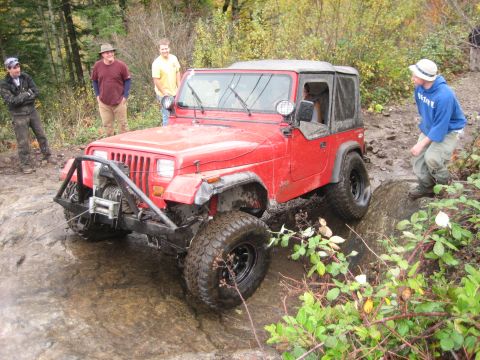 1990 Ford Bronco - A red Jeep Wrangler tackles a challenging off-road course, demonstrating its capabilities.