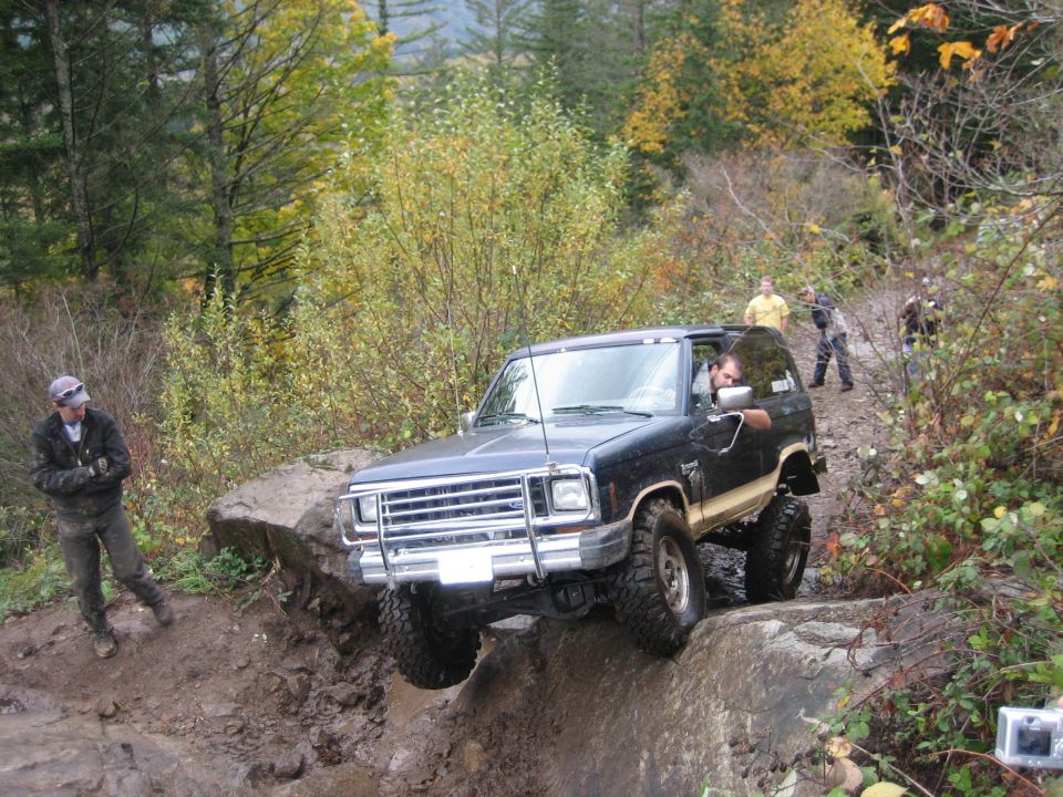 Black Ford Bronco off-roading on a rocky, muddy trail with a person standing nearby
