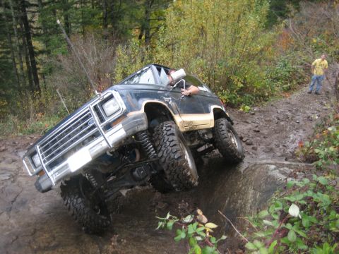 1990 Ford Bronco - A modified SUV navigates a challenging off-road course with a person watching in the background.