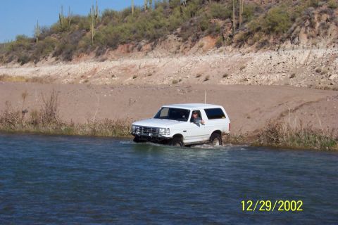 1993 Ford Bronco - White 1993 Ford Bronco navigates through a body of water in a desert landscape.