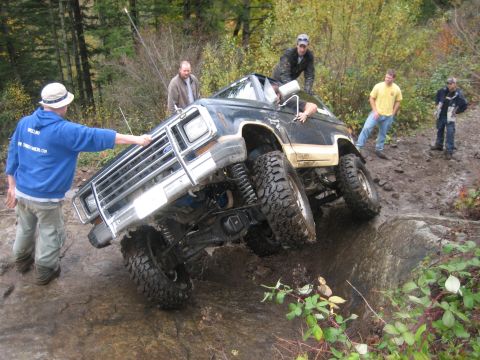 1990 Ford Bronco - A black Ford Bronco navigates a challenging off-road obstacle with several people observing.