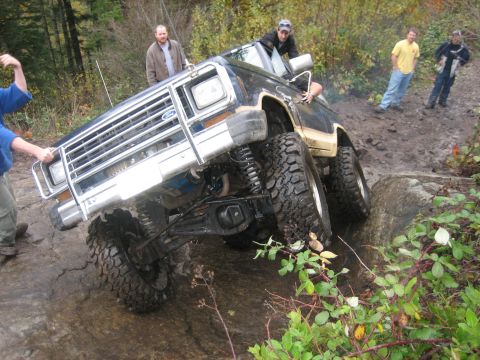 1990 Ford Bronco - This modified SUV is shown tackling a challenging rocky terrain, with several people observing and assisting.