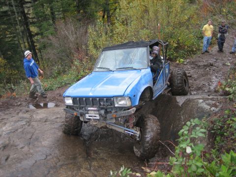 1990 Ford Bronco - This modified SUV is tackling a challenging off-road course with spectators observing the action.