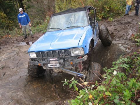 1990 Ford Bronco - A blue off-road vehicle navigates a challenging rocky and muddy terrain.