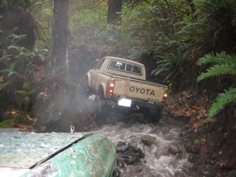 1990 Ford Bronco - Toyota pickup truck driving through a stream in a wooded area. Another vehicle is in the foreground.