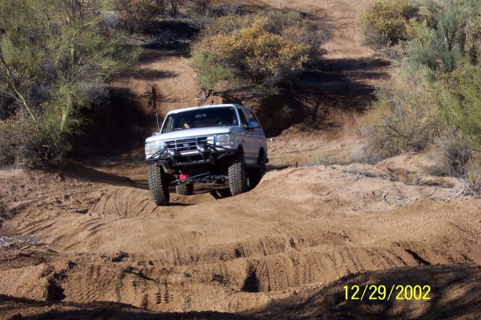 White lifted full-size Ford Bronco jumping on a desert dirt trail