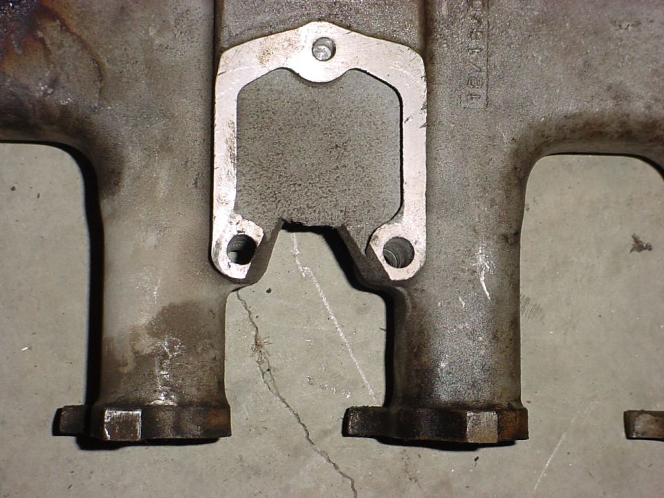 Close-up of two exhaust manifold pipes with a gasket in between. Text on the manifold reads 'D6TE12A'