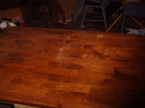 1988 Ford Bronco - A wooden table with visible water damage and scratches is shown, with chairs in the background.