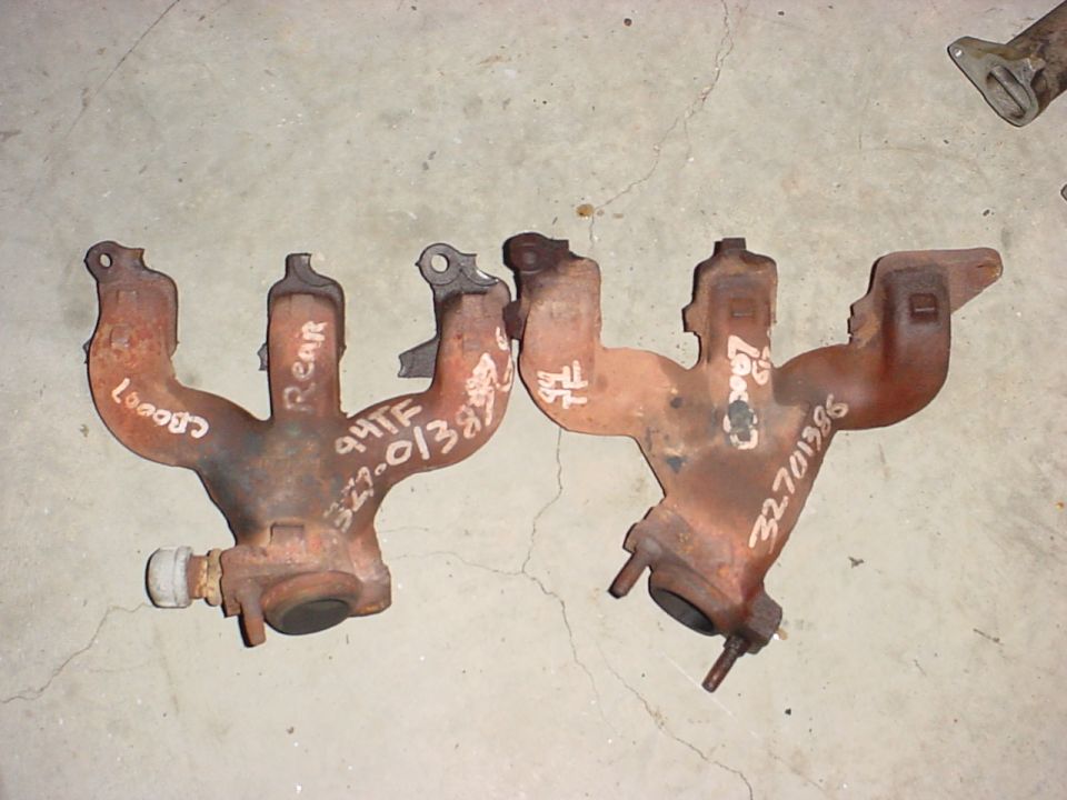 Two rusty exhaust manifolds with white markings and part numbers