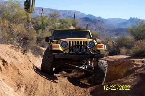 1993 Ford Bronco - Yellow Jeep Wrangler navigating a rough desert terrain on a sunny day.