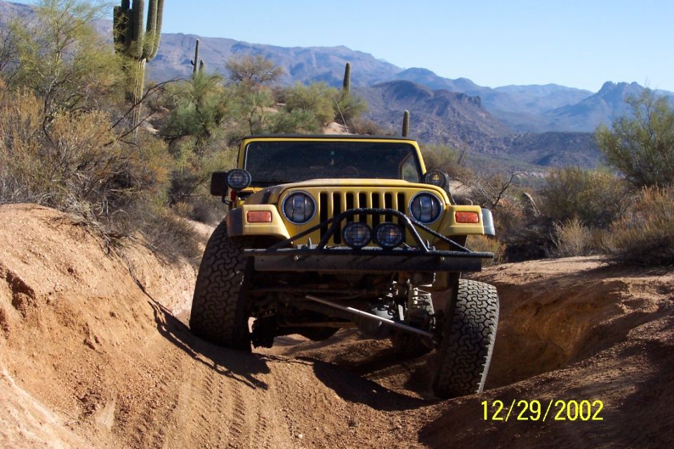 Yellow open-top Jeep Wrangler flexing over a dirt berm on a saguaro desert trail