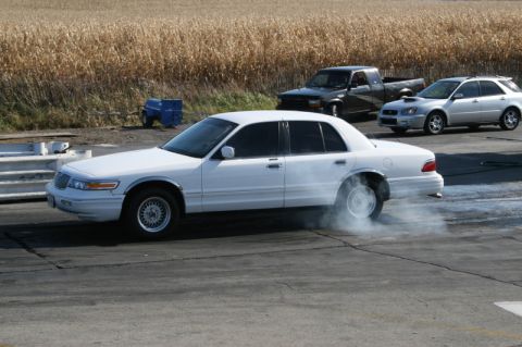 1997 Mercury Grand Marquis - White 1997 Mercury Grand Marquis performing a burnout on a track, with other vehicles visible.