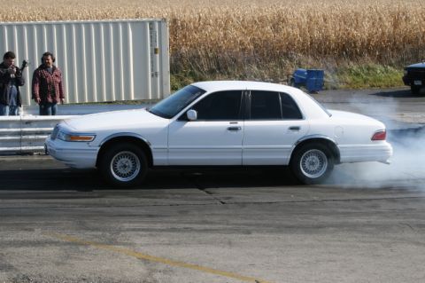 1997 Mercury Grand Marquis - White full-size Mercury sedan doing a tire-smoking burnout in the water box at a drag strip, shot broadside with the rear tires clouded in…