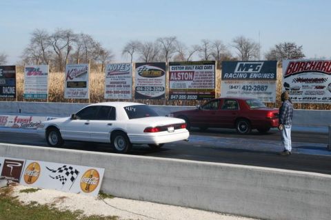 1997 Mercury Grand Marquis - Two sedans are lined up on a drag strip, with advertising banners in the background.