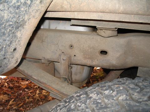 1984 Ford Bronco - The undercarriage of a vehicle, a worn frame and suspension system, is visible in this close-up shot.