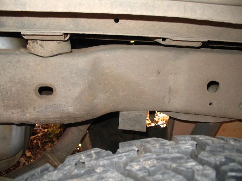 1984 Ford Bronco - A close-up view of a vehicle's undercarriage, focusing on the frame and a tire, reveals significant rust and wear.