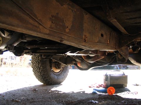 1984 Ford Bronco - The underside of a vehicle reveals significant rust on the frame and suspension parts.