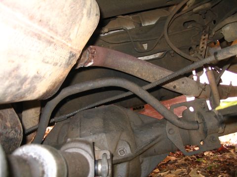 1984 Ford Bronco - The underside of a vehicle shows a rusted exhaust pipe connected to the rear axle assembly.