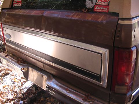 1984 Ford Bronco - Rear view of a brown 1980 Ford Bronco showing its tailgate, bumper, and stickers on the window.