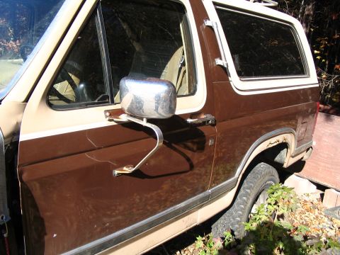 1984 Ford Bronco - A brown and tan Ford Bronco shows signs of wear and tear, with visible rust and cracked paint on its side.