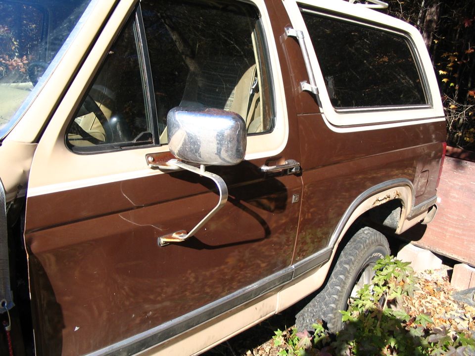 Brown and tan Ford Bronco side view, showing rust on wheel well, cracked paint, and a chrome side mirror