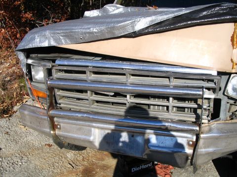 1984 Ford Bronco - The front grille and bumper of a truck, possibly from the 1980s, are visible beneath a tarp.