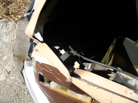 1984 Ford Bronco - The front end of a vehicle shows significant damage, with the hood open to reveal the dark engine compartment.