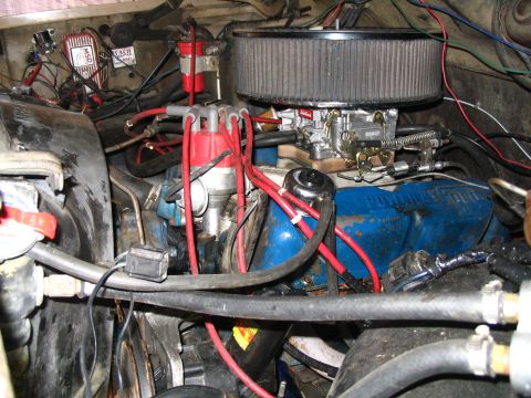 1984 Ford Bronco - The engine bay of a 1984 Ford Bronco shows a blue engine block, red spark plug wires, and a prominent air filter.